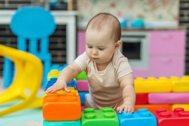 Kapalı alanda oynarken geniş renkli plastik bloklara dokunan meraklı çocuk, odak, keşif, erken gelişim ve çocukluk öğrenme faaliyetlerini gösteriyor.