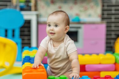 Gülümseyen çocuk, parlak bir oyun odasındaki büyük plastik yapı taşlarının arasında durmuş neşe, yaratıcılık ve erken çocukluk zamanlarını kapalı alanlarda gösteriyor..