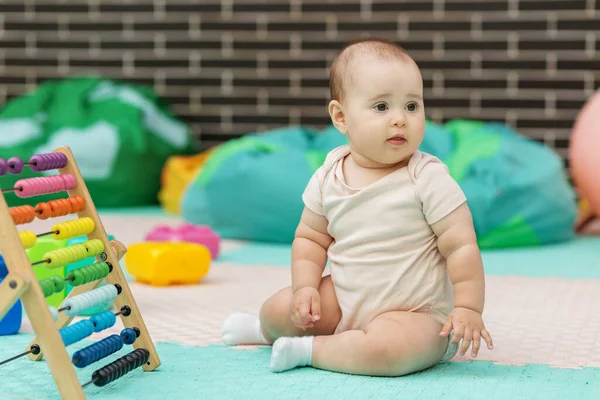 Bebek parlak bir oyun odasında renkli abaküsün yanında yumuşak köpüklü mindere oturur. Eğitim, kreş ve çocuk gelişimi konuları için ideal.