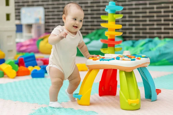 Mutlu bebek öğrenme oyuncaklarıyla dolu güvenli bir kreşte renkli bir oyuncak masasının yanında ilk adımlarını atıyor..