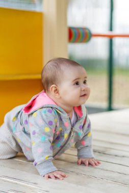 Gülen kız puantiyeli kapüşonlu bebek oyun alanı ekipmanlarının yanında tahta zeminde sürünüyor, güvenli bir ortamda oyun zamanının tadını çıkarıyor..
