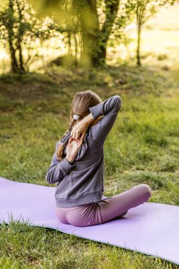 Genç bir kız, bir sonbahar parkında, bir yoga minderinde, esneklik, zindelik ve sağlığa odaklanmış bir şekilde kol esnetme çalışması yapıyor..