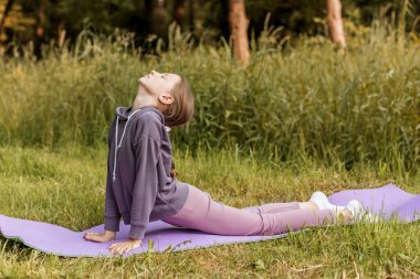 Kobra pozuyla yoga yapan bir çocuk, esnekliği, farkındalığı ve doğada sağlıklı bir yaşam tarzını teşvik ediyor..