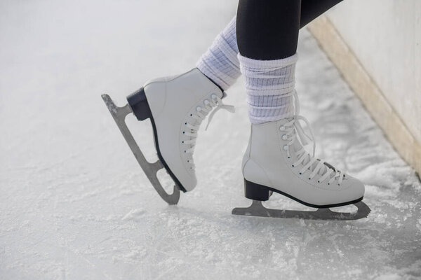 Close-up of white figure skates with Cyrillic text, worn on a frozen outdoor rink with visible ice texture and snow.