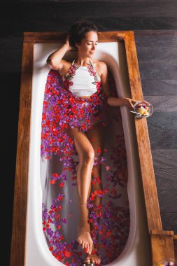 Genç kız beyaz banyo çiçeklerle yalan yukarıdan görüntüleyin. Koyu ahşap iç oda içinde