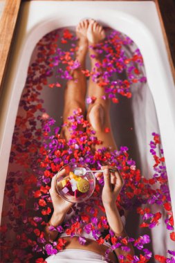 Kadın ayakları çiçek Bath Spa. Plaka ile taze meyve salatası, holding eller görüntülemek yukarıdan