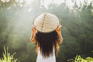Geleneksel balinese hasır şapkalı uzun kıvırcık saçlı kadın arkadan görünüş.