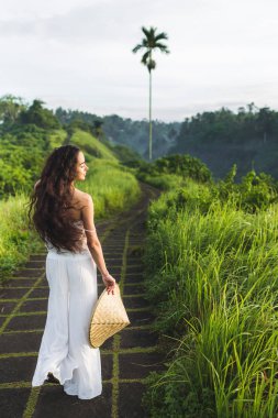 Hasır şapka sanatçılar, Ubud, Bali Campuhan Ridge yolu üzerinde poz tutarak uzun saçlı kadın görünümünü arka.