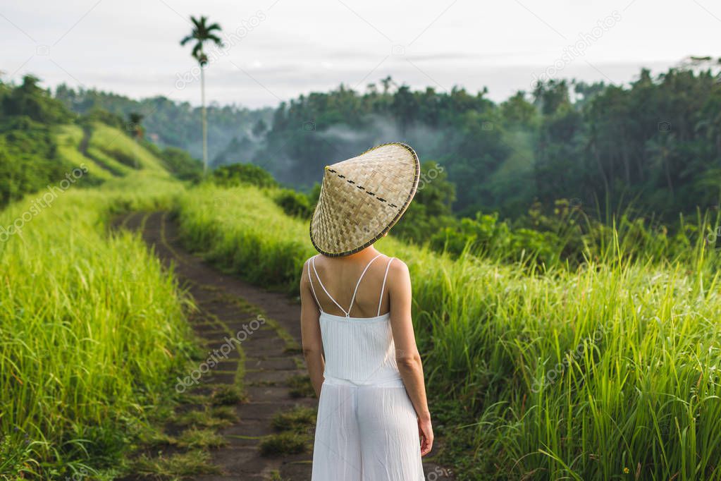 Rear view of woman in asian straw hat walking on Campuhan Ridge way of artists, Ubud, Bali.