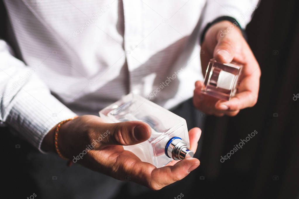 Man holding bottle of perfume and smelling fragrance, close-up 