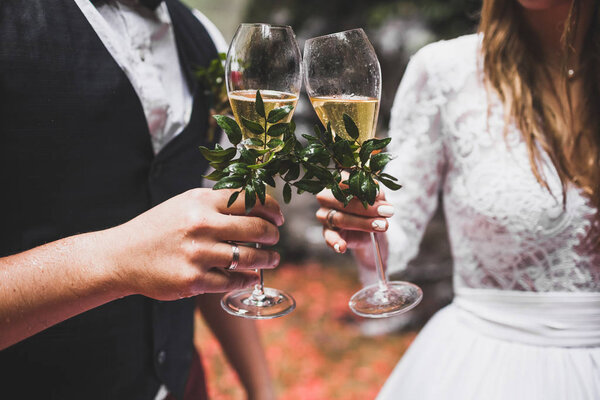 Man and woman hands holding two champagne glasses decorated with flowers for wedding ceremony