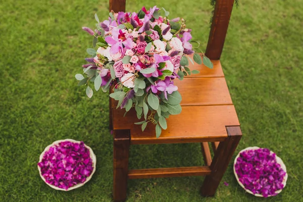 結婚式の芝生の上に立っている茶色の木製の椅子はピンクと紫の花で飾られました 花びらとプレート — ストック写真