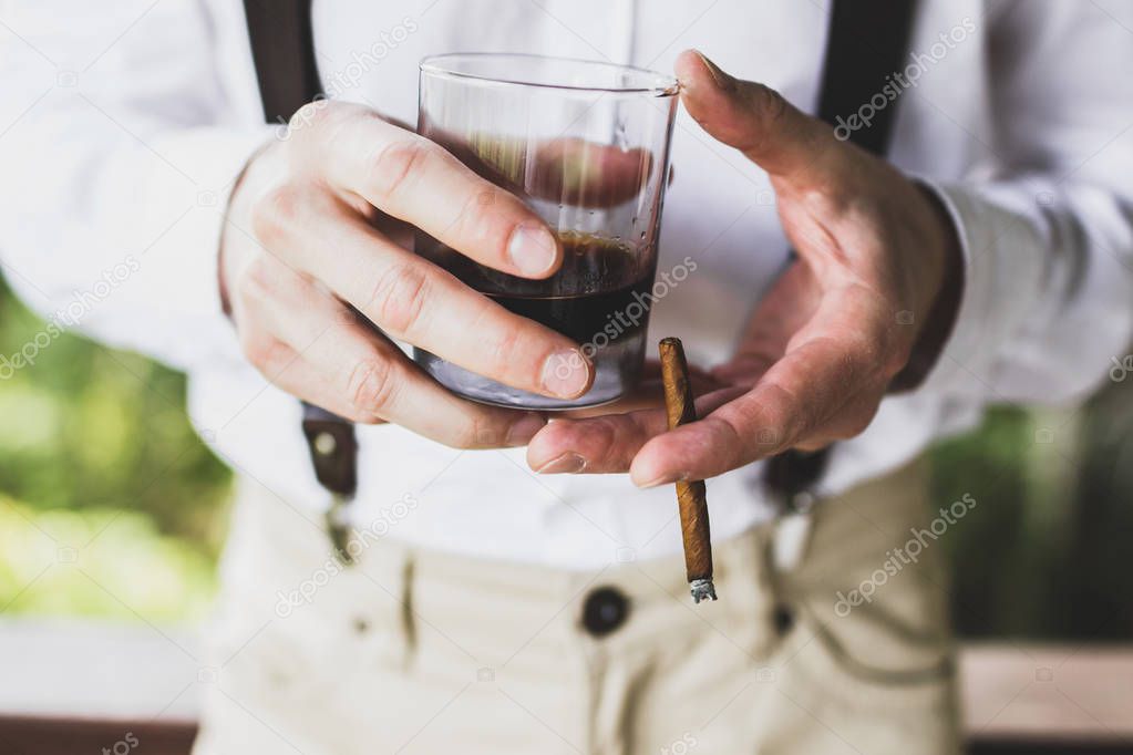 Man holding in hands glass of whisky and cigar
