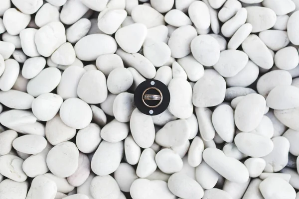白い小石石の背景に円形のブラック ボックスでの結婚指輪 — ストック写真
