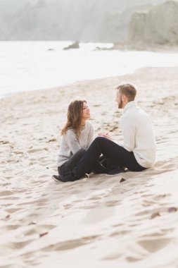 Happy man and woman sitting on sand near sea, romantic mood clipart