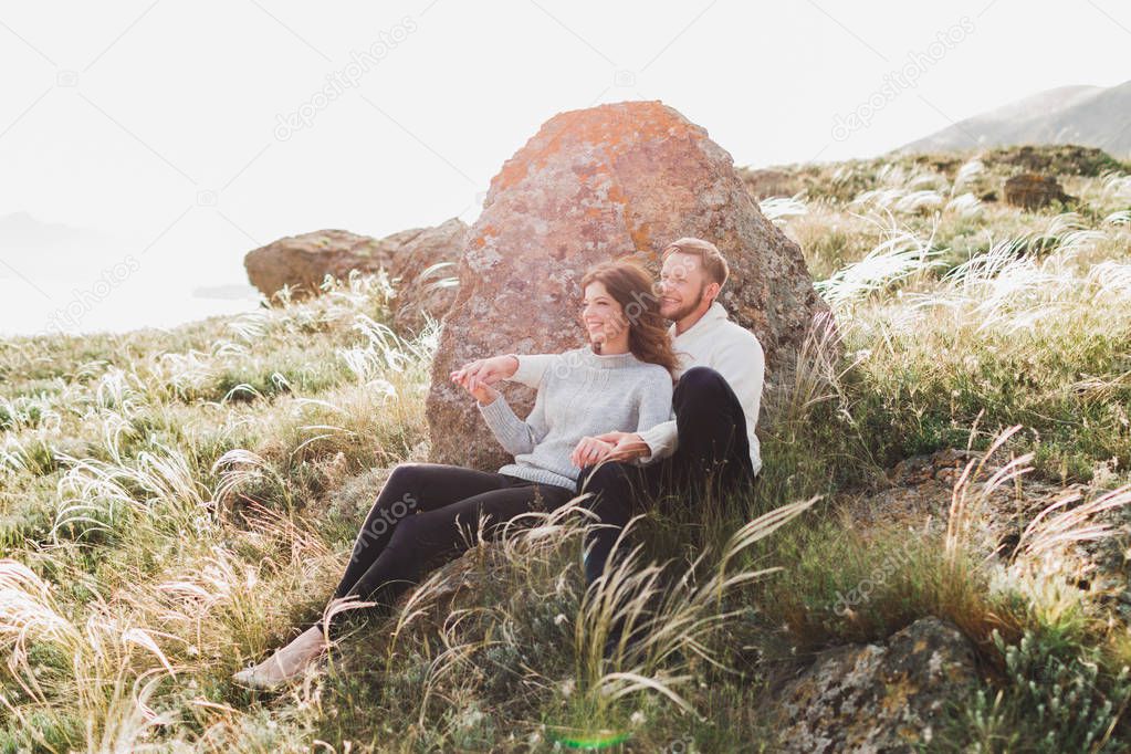 Happy young loving couple sitting in feather grass meadow, laughing and hugging, casual style sweater and jeans