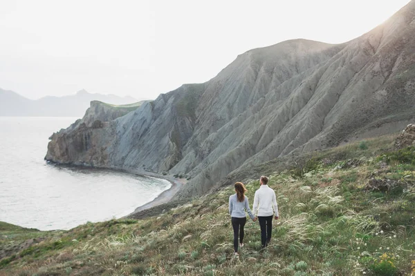 Young couple walking on nordic sea coast with mountain view in spring, casual style clothing sweaters and jeans