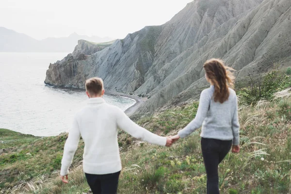 Young couple walking on nordic sea coast with mountain view in spring, casual style clothing sweaters and jeans