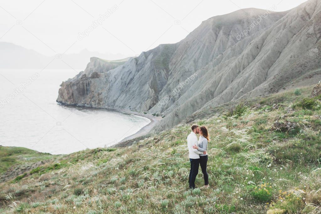 Young couple walking on nordic sea coast with mountain view in spring, casual style clothing sweaters and jeans