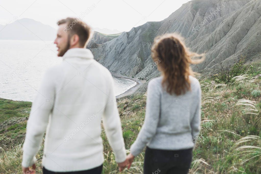 Young couple walking on nordic sea coast with mountain view in spring, casual style clothing sweaters and jeans