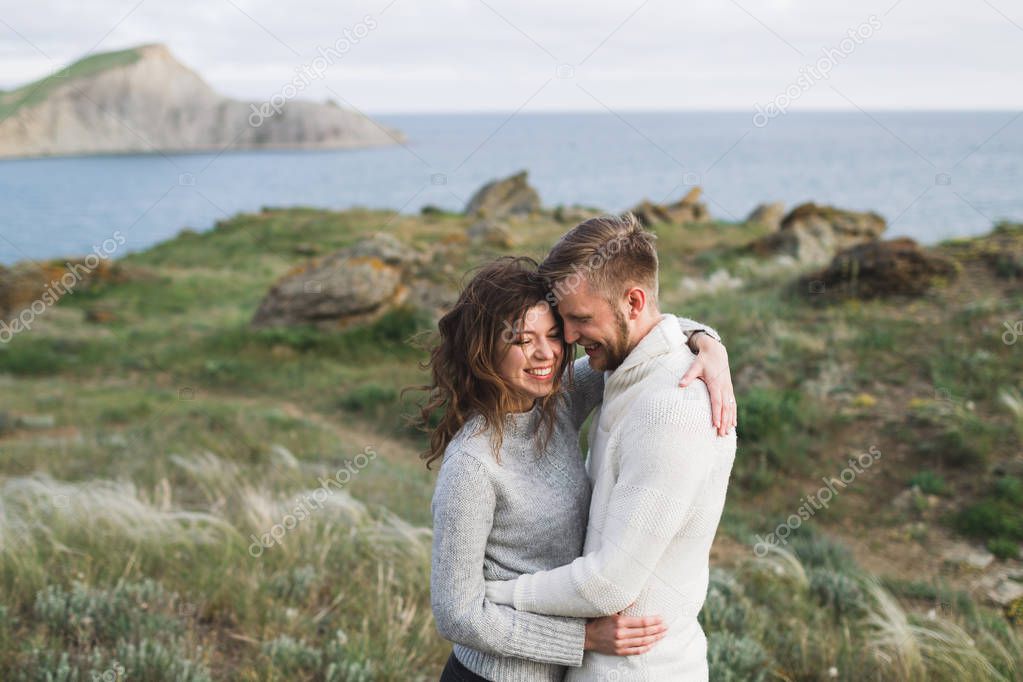 Young couple walking on nordic sea coast with mountain view in spring, casual style clothing sweaters and jeans