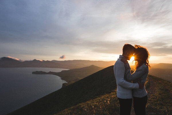 Счастливая пара обнимается и целуется на закате с потрясающим видом на горы. Теплый вечерний солнечный свет
