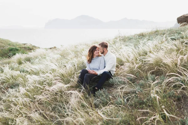 幸せな若いカップル羽草草原に座って 笑って カジュアルなスタイルのセーターとジーンズを愛する — ストック写真