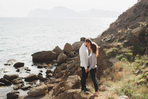 Young couple walking on nordic sea coast with mountain view in spring, casual style clothing sweaters and jeans