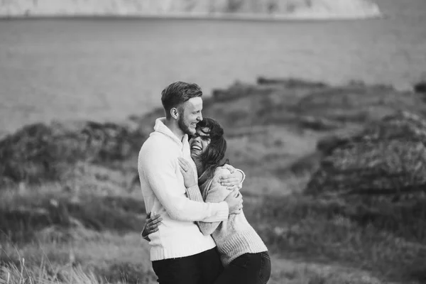 Young couple walking on nordic sea coast with mountain view in spring, casual style clothing sweaters and jeans. Black and white toning