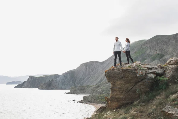 年轻夫妇走在北欧海岸与山景在春天 休闲风格的服装毛衣和牛仔裤 — 图库照片