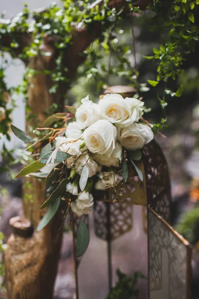 Wedding ceremony decoration with white rose composition and vintage bronze hanging lamp on branch with ivy