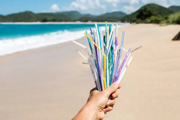 Tangan memegang tumpukan sedotan plastik bekas di latar belakang bersih — Stok Foto