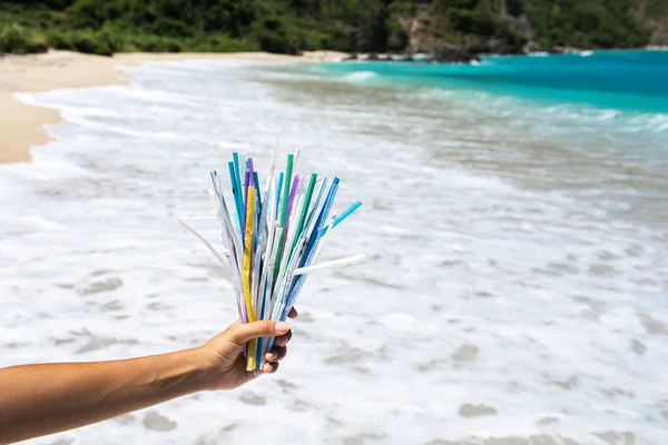 Hand holding heap of used plastic straws on background of clean