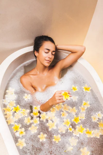 Asian woman enjoying in flower bath with foam, bubbles and yello