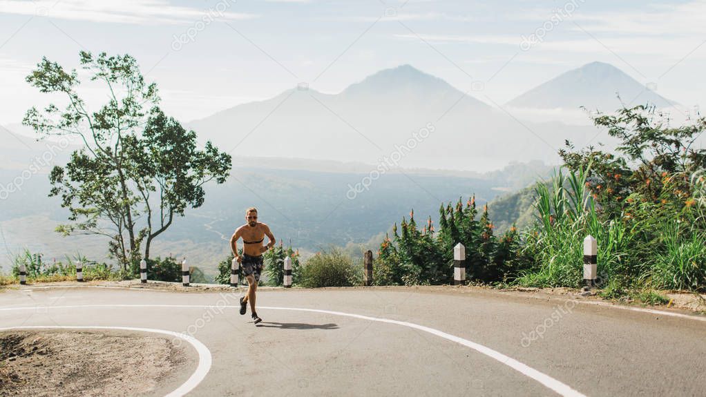 Man running topless in uphill on the asphalt road in hot summer 