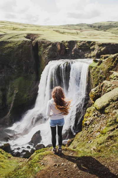 Lockig kvinna som tittar på Fagrifoss vattenfall på Island. Utsikt från — Stockfoto