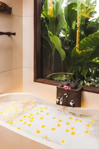 Bañera con burbujas de espuma y flores amarillas con garde tropical — Foto de Stock