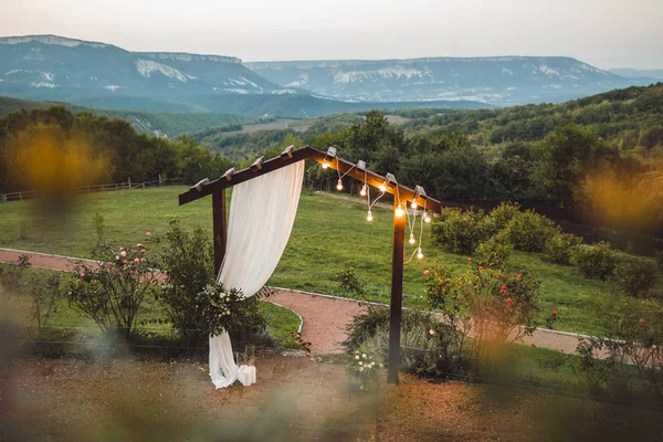 Arco de boda de madera con paño blanco y bombillas al aire libre wi —  Fotos de Stock