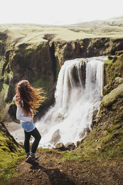 Kudrnatá žena, která hledí na Fagrifoss vodopád na Islandu. Zobrazit z — Stock fotografie