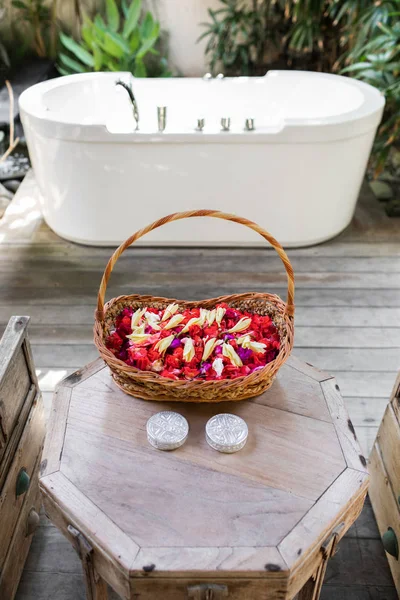 Wooden wicker basket with red and white flower petals in front o — Stock Photo, Image