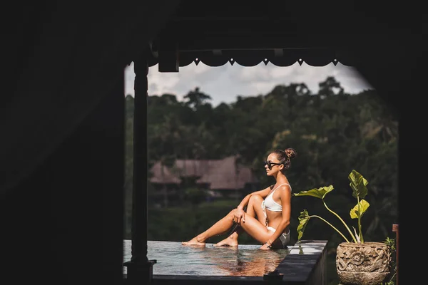 Женщина в белых купальниках и солнцезащитных очках расслабляется в роскошном инфинити — стоковое фото