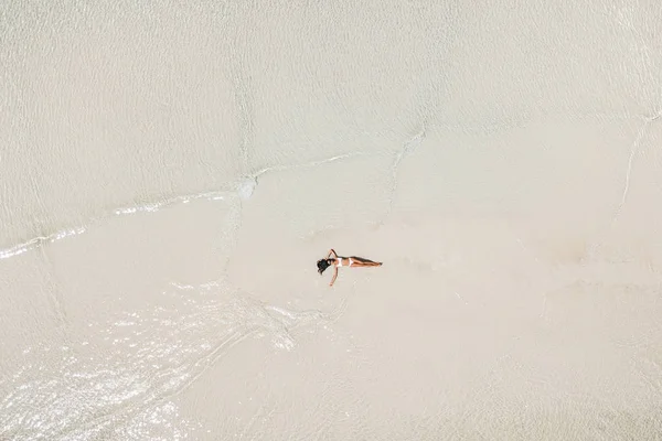 Aerial drone shot of woman lying in water on white sand beach an — Stock Photo, Image