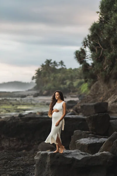 Jovem mulher grávida em vestido branco desfrutando de noite em Bali bea — Fotografia de Stock