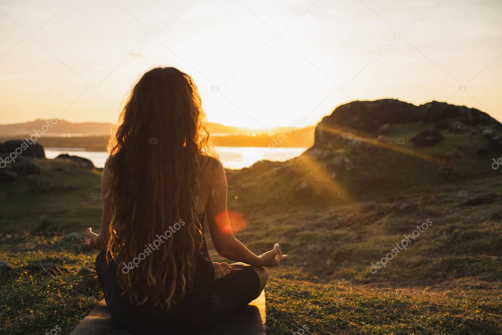 Woman meditating yoga alone at sunrise mountains. View from behi