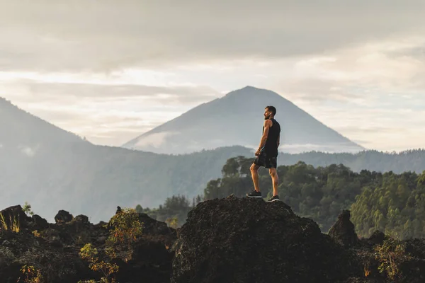 Молодой человек стоит на камне и наслаждается удивительным вулканом — стоковое фото