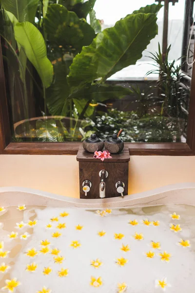 Ванна з бульбашками піни і жовтими квітами з тропічним гардеробом — стокове фото