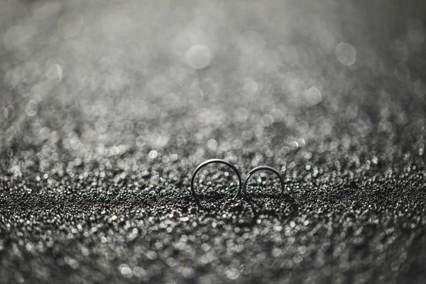 Nahaufnahme von zwei Eheringen Ionenhintergrund aus schwarzem Sand. — Stockfoto