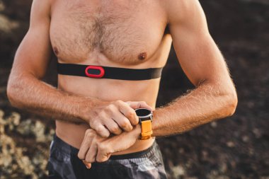 Atletik adam akıllı saat veya fitness izci programı çalışan başlar. Eğitim üstsüz ve göğüs kalp hızı monitörü kullanarak. Vücut yakın çekim.