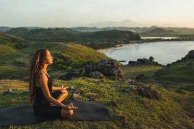 Woman doing yoga alone at sunrise with mountain and ocean view.  clipart