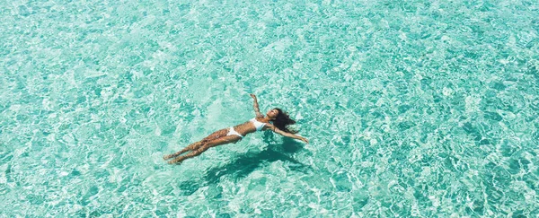 Mulher de biquíni branco deitada em surfa de água azul-turquesa transparente — Fotografia de Stock